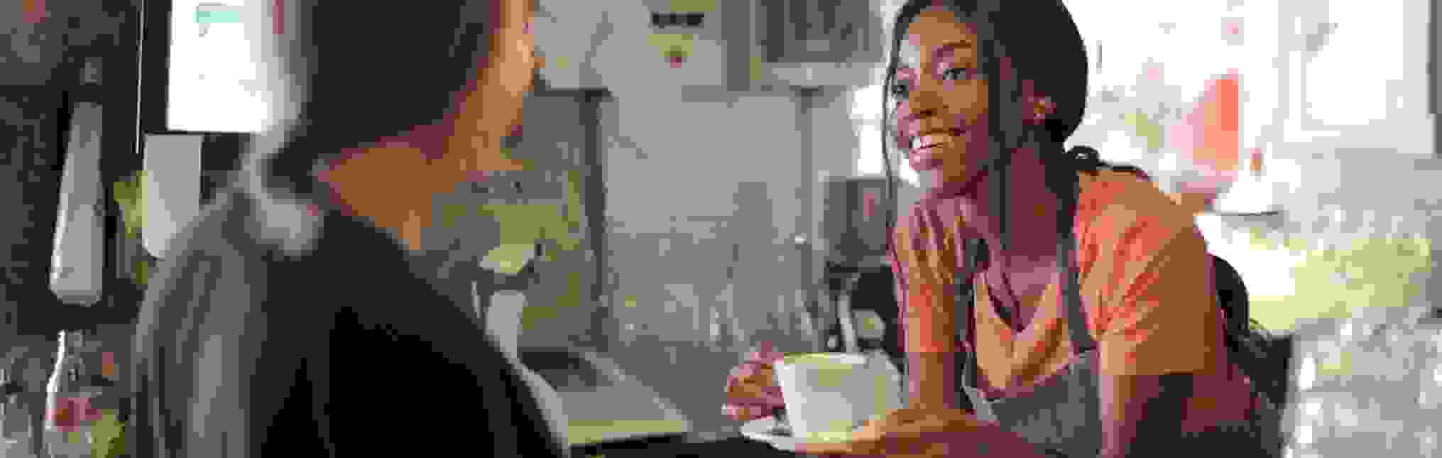 Delighted black female barista serving coffee in cup in cafe