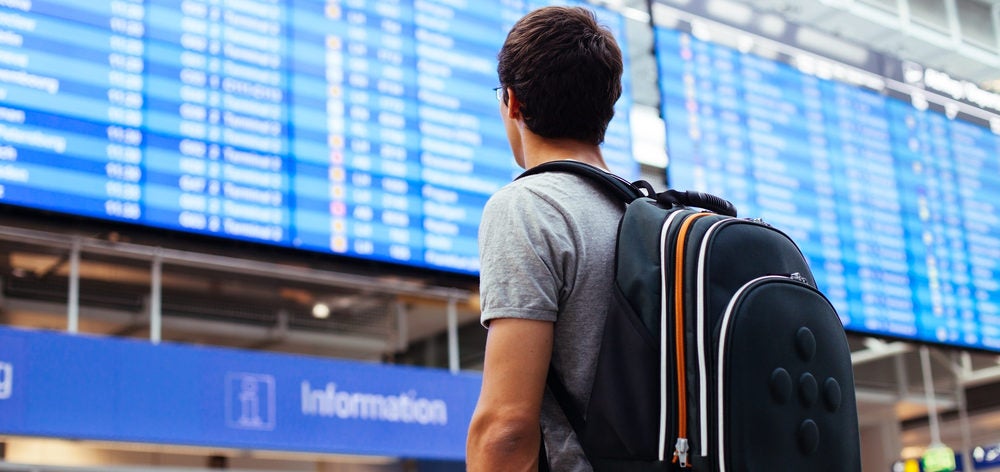 man backpack looking at airport board delay