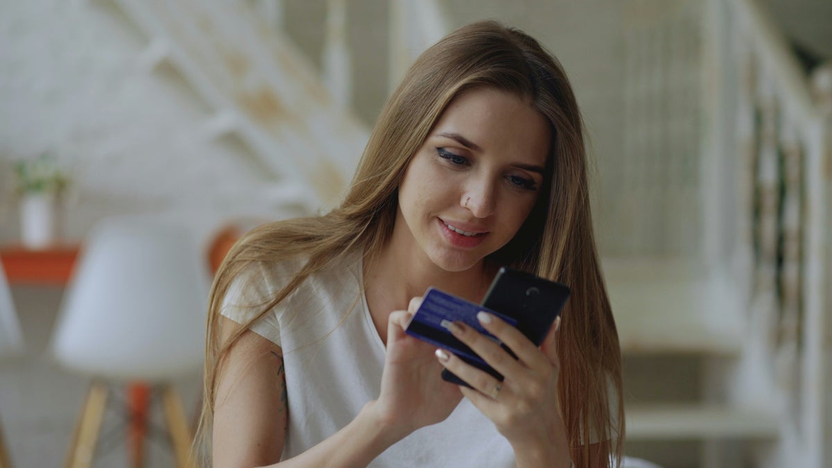 Happy woman with credit card looking at phone