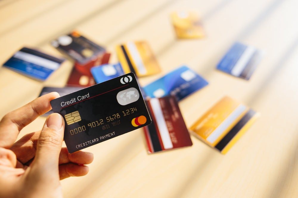  A person's hand holding a black credit card in front of a wooden table scattered with other credit cards representing the timeline for a credit card application.