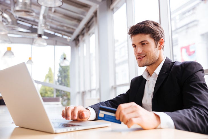 Happy young businessman using laptop and credit card at the table