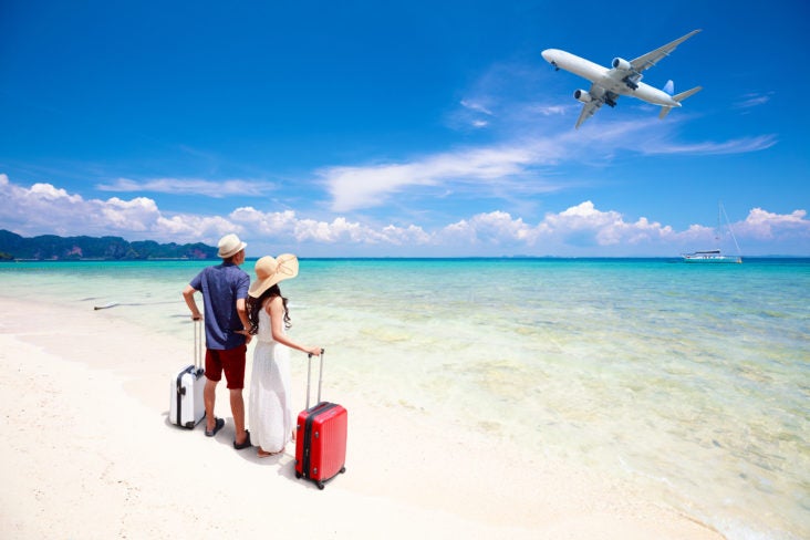 couple with luggage on beach looking at an airplane couple with luggage on beach looking at an airplane