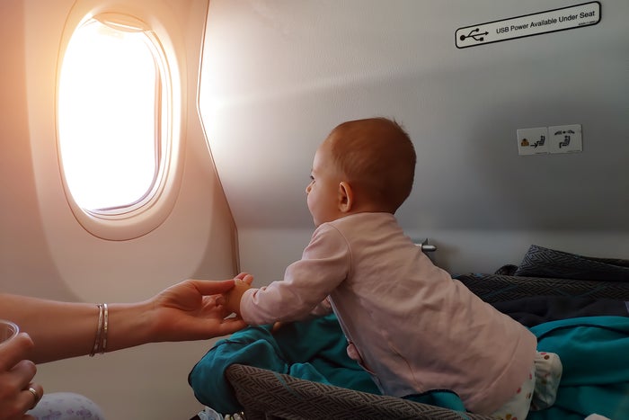 Baby looking out airplane window in bassinet