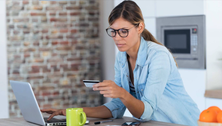Shot of woman using her laptop for shopping online and paying with credit card while sitting in the kitchen at home Shot of woman using her laptop for shopping online and paying with credit card while sitting in the kitchen at home