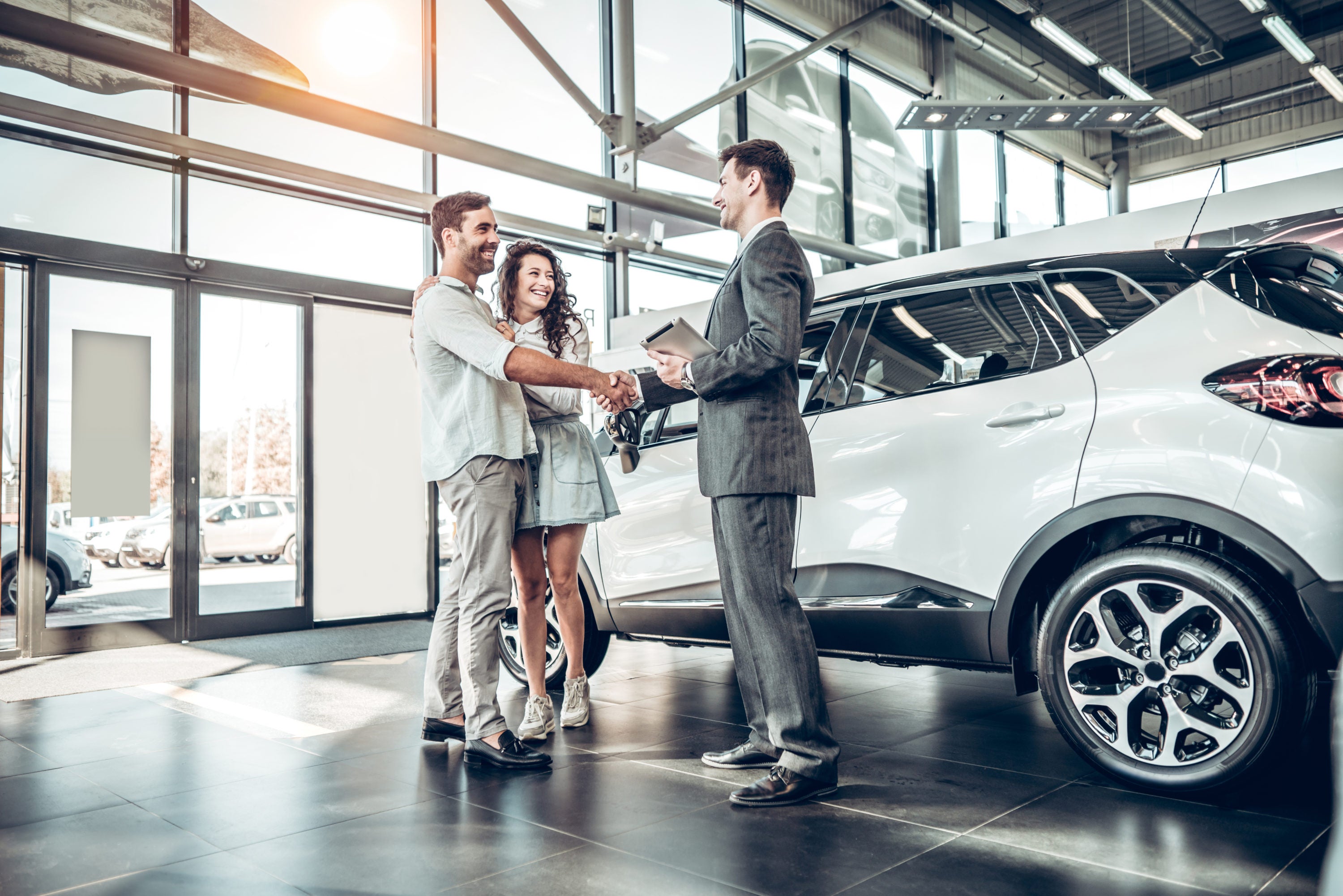 Purchasing a car at dealer couple shaking salesperson's hand