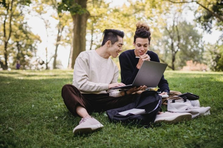 College students on grass with laptop and bags College students on grass with laptop and bags