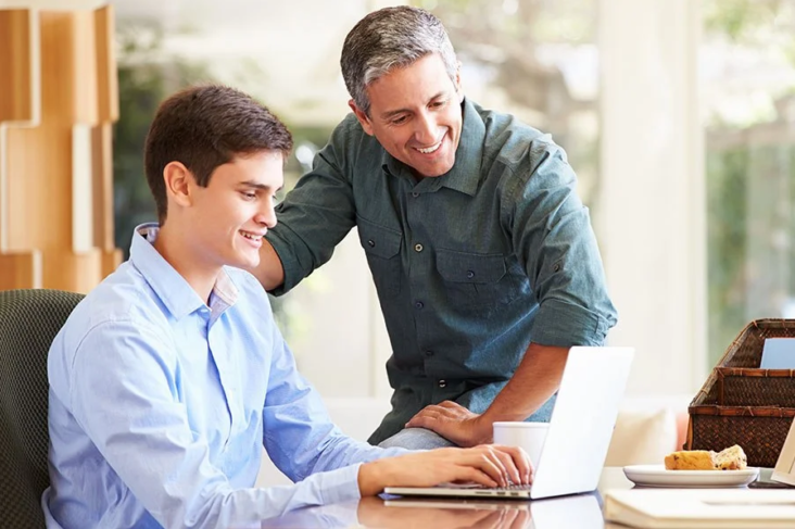 Father And Teenage Son Looking At Laptop Together Father And Teenage Son Looking At Laptop Together
