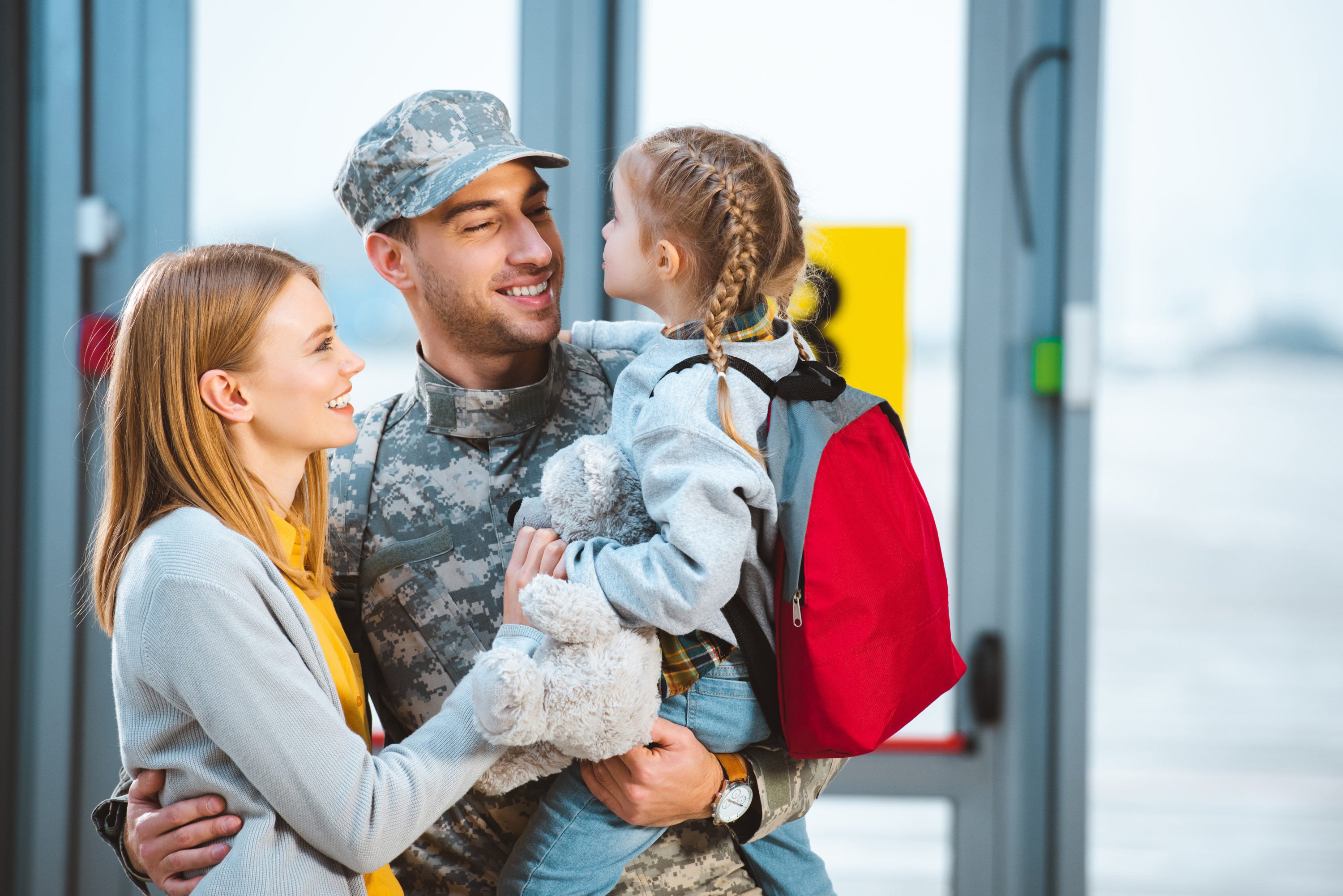 Smiling father in military uniform holding in arms daughter near wife in airport