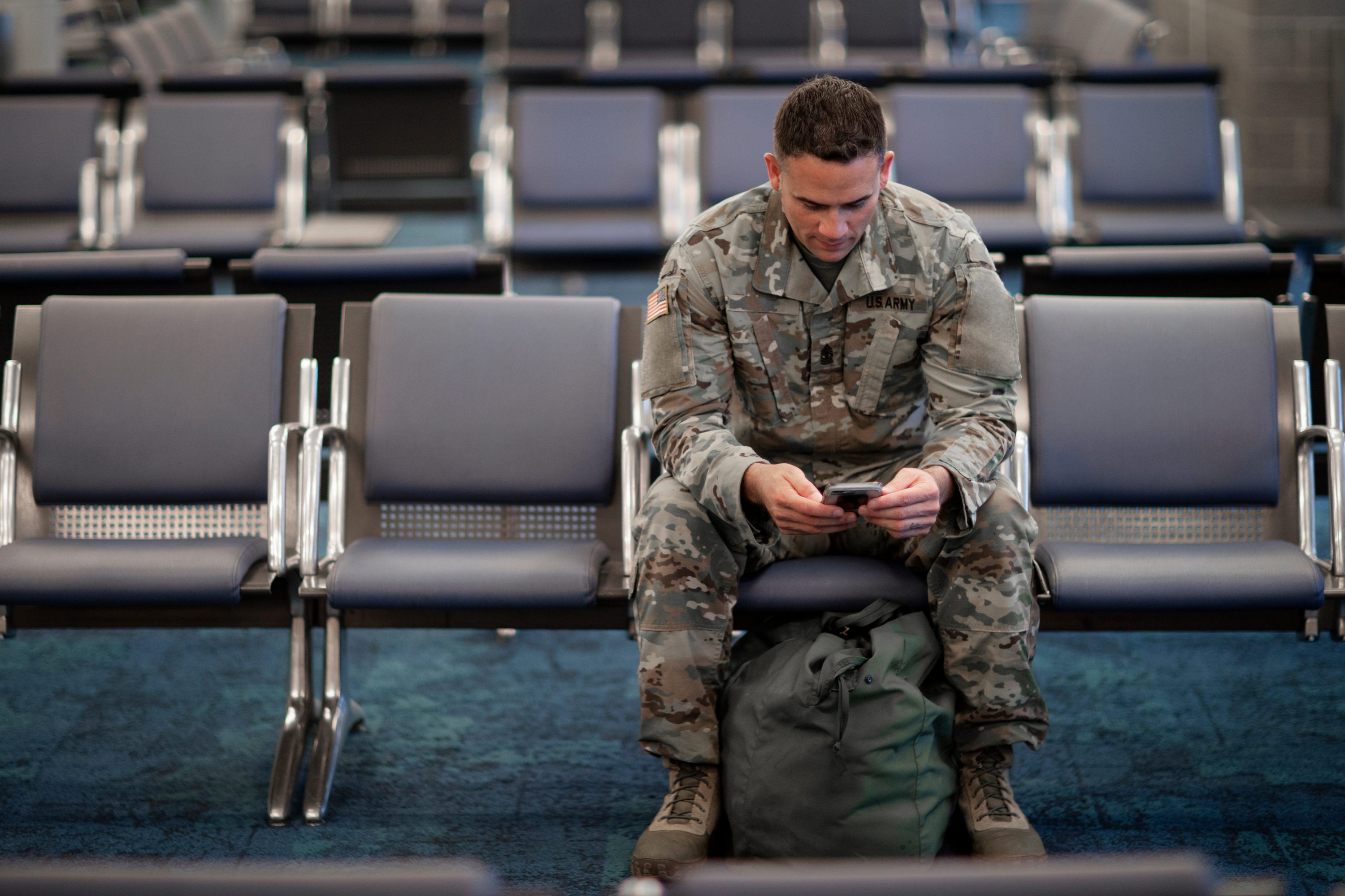 Soldier looking at his cell phone while waiting at an airport