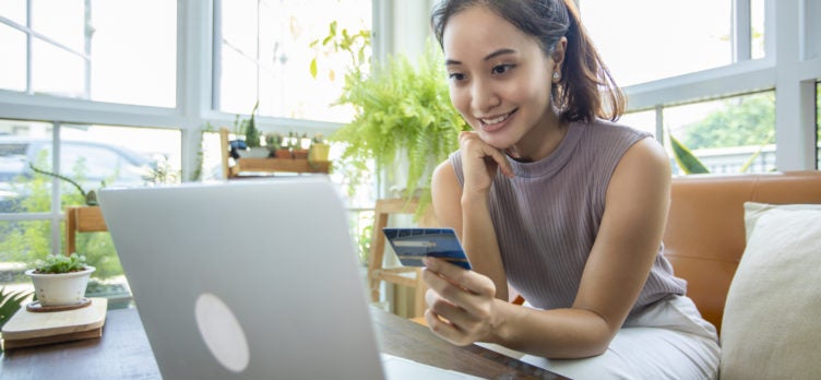 Woman is holding credit card and using smartphone shopping online at home