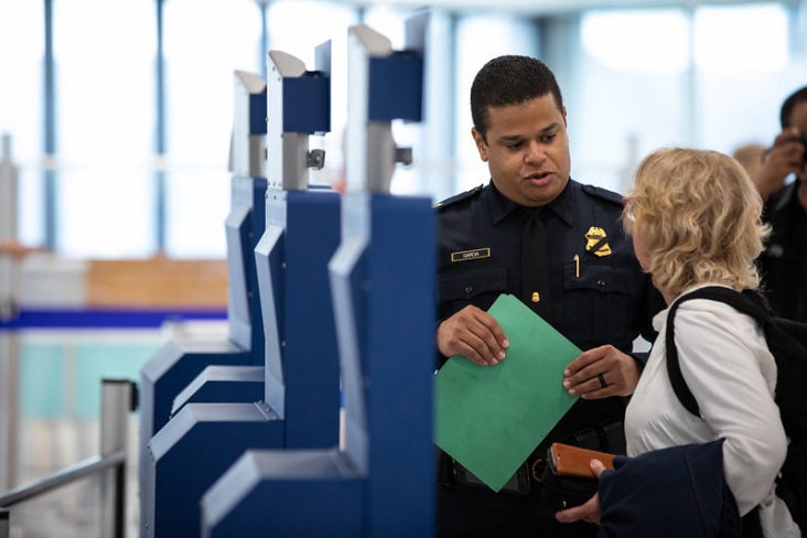 Man in hat using Global Entry kiosk Woman using Global Entry kiosk with CBP agent