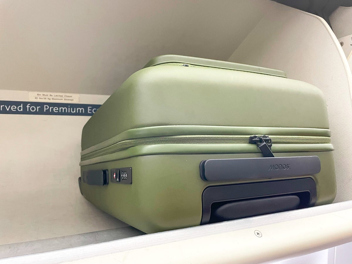 Olive Green Monos Luggage in Amerian Airlines overhead bin handle