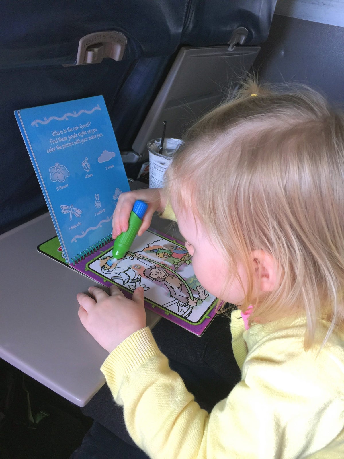 Child drawing in a coloring book while seated on an airplane.