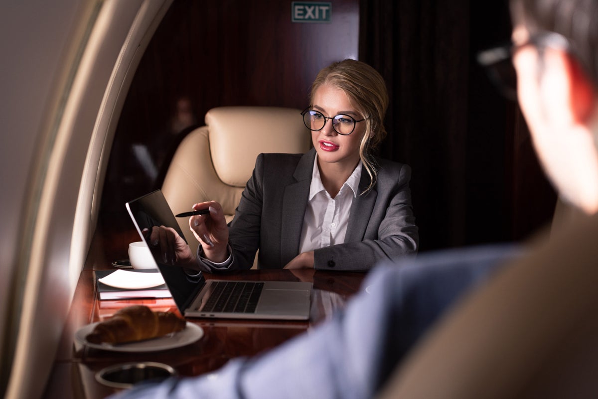 Businesswoman on private jet pointing at laptop