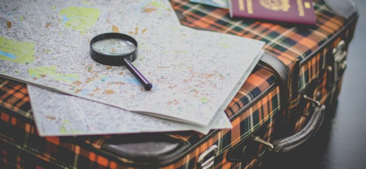Maps and magnifying glass with passport on suitcase
