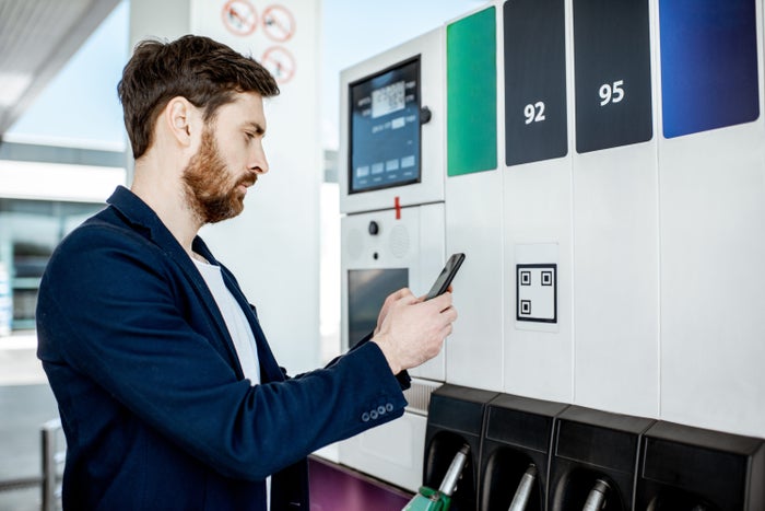 Man paying with phone for gasoline, photographing bar code on the gas station pump