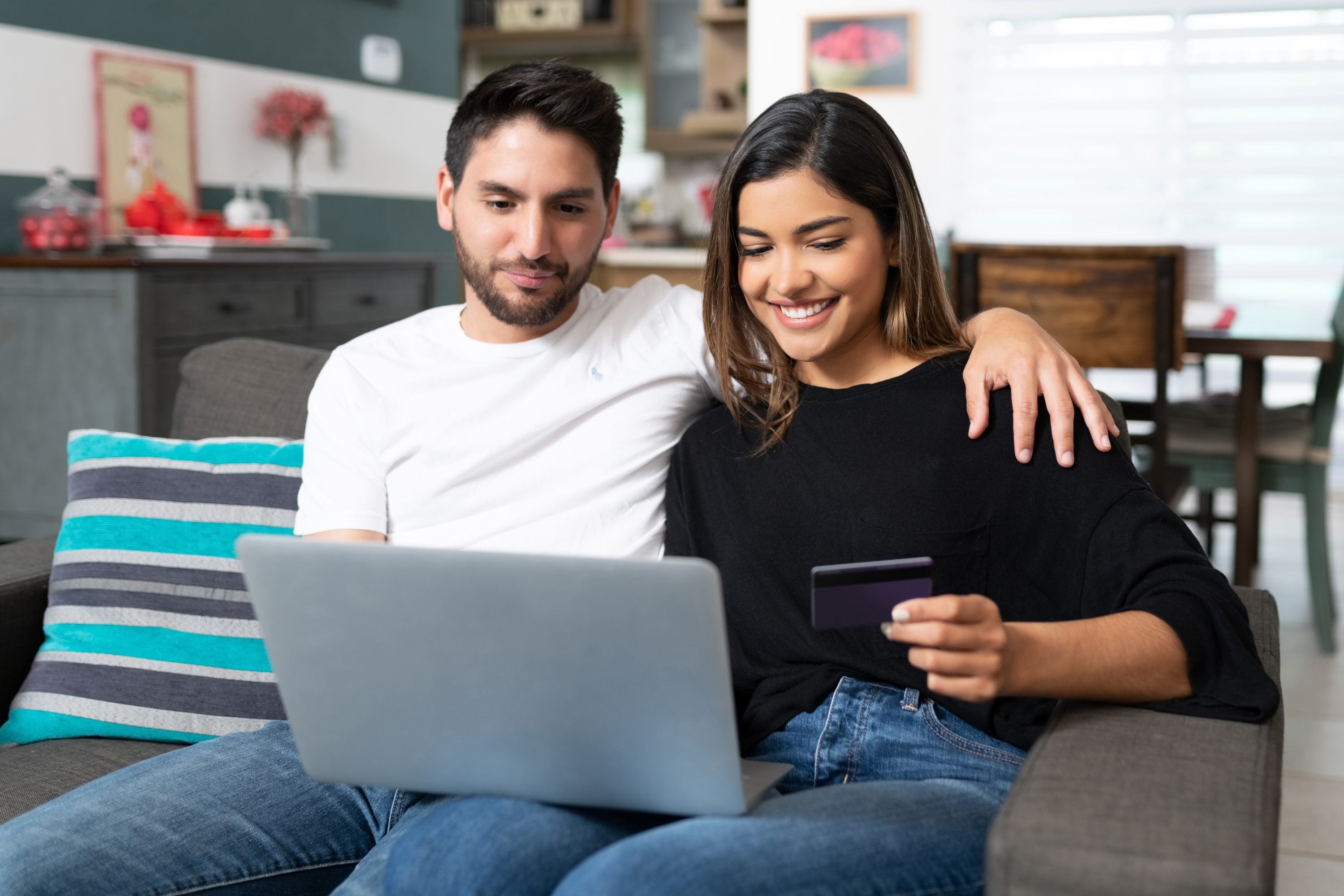 Happy couple shopping online through laptop while sitting on sofa in living room at home