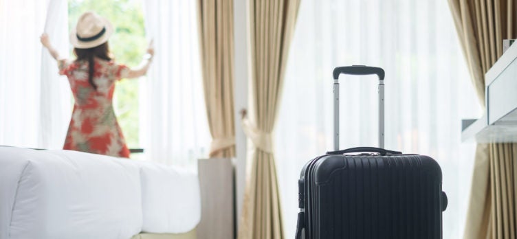 Luggage in modern hotel room with happy young adult female relaxing nearly window