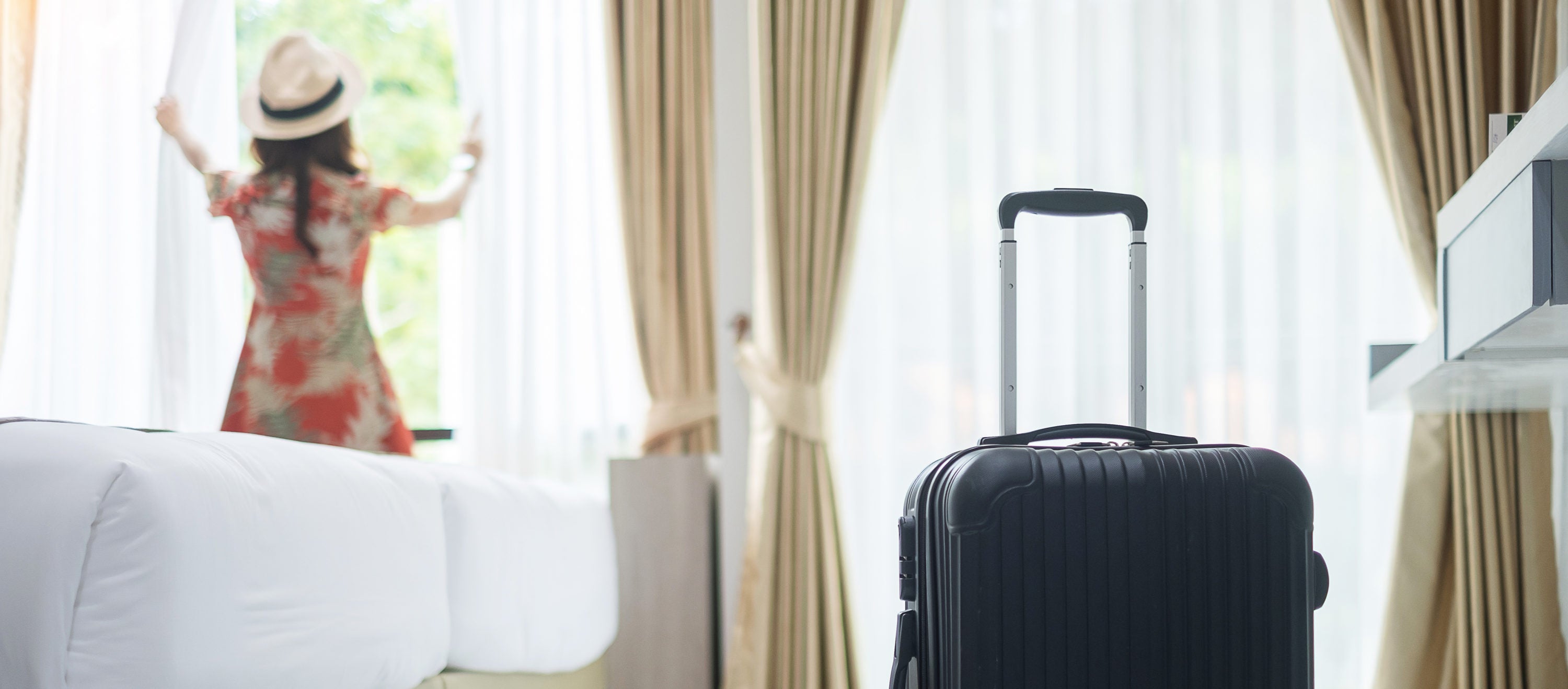 Luggage in modern hotel room with happy young adult female relaxing nearly window
