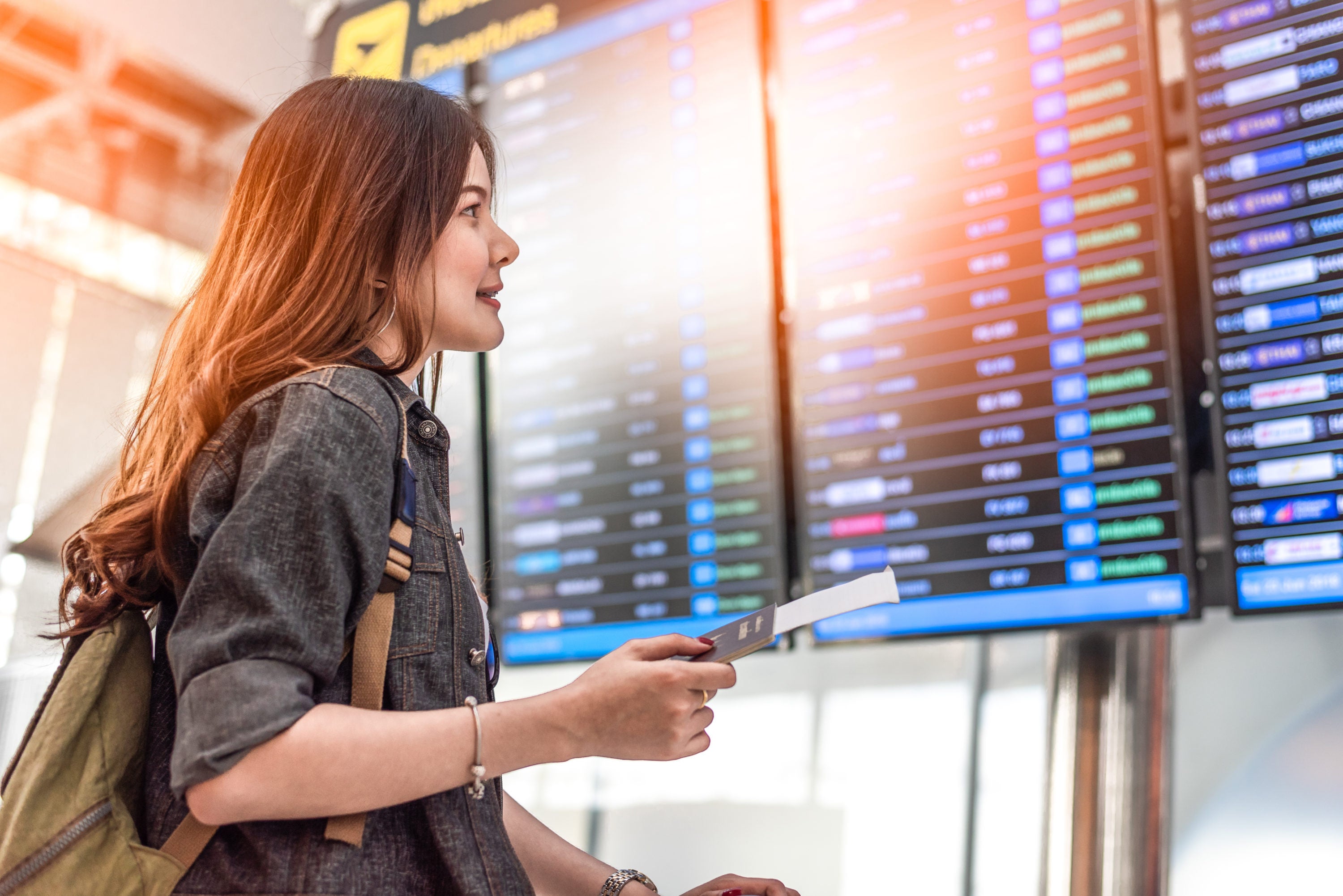 Female traveler looking at airline departure board at airport with passport