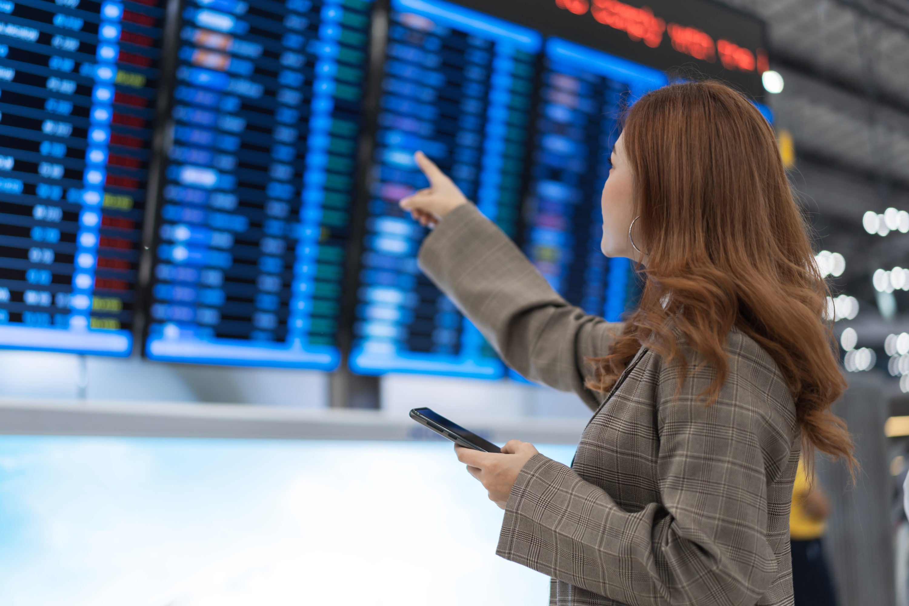 Female traveler pointing at airline departure board at airport