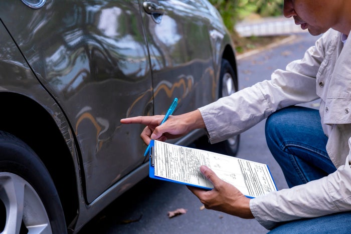 Insurance agent writing on clipboard while examining car after accident claim being assessed and processed