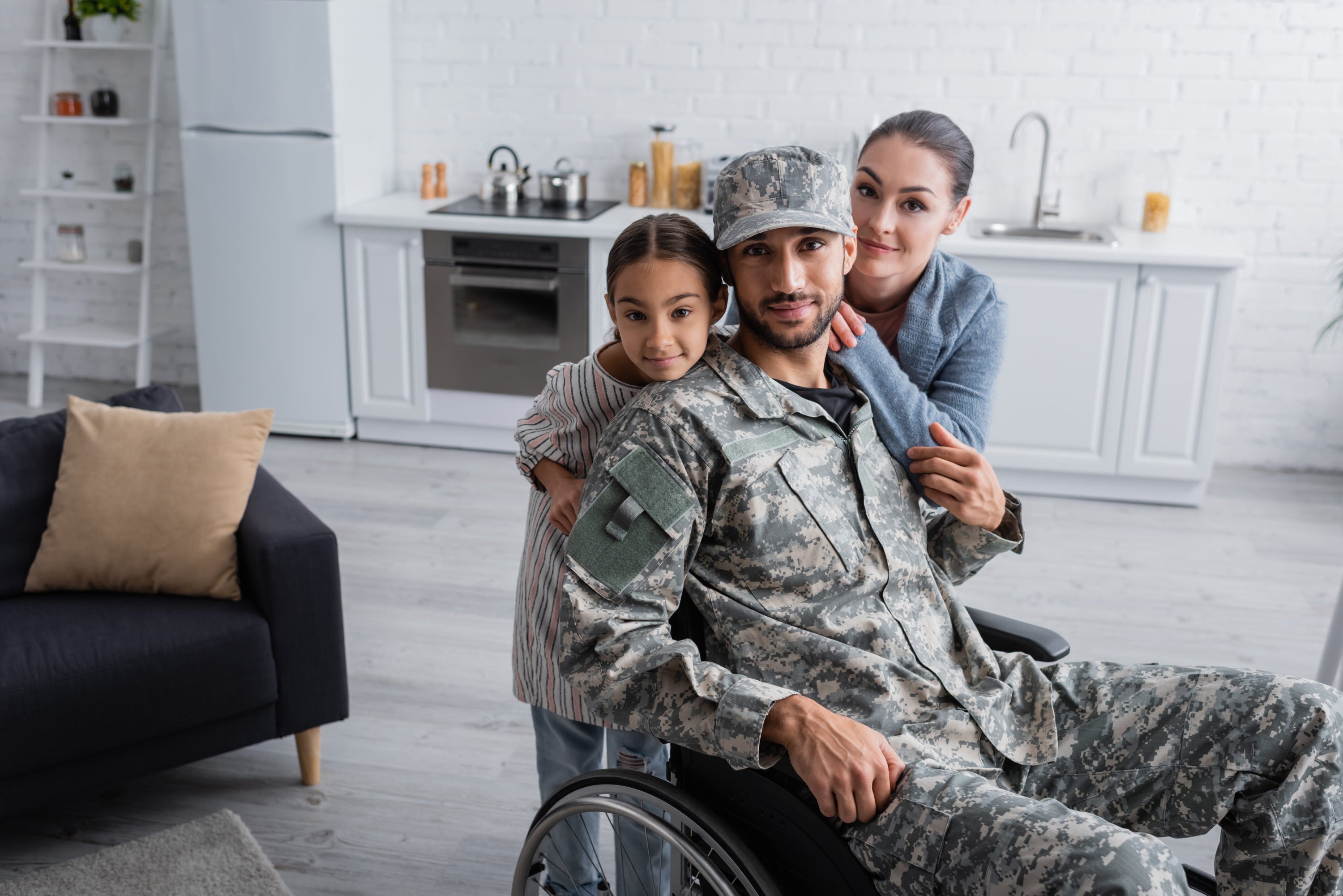 Man in military uniform and wheelchair looking at camera near family at home