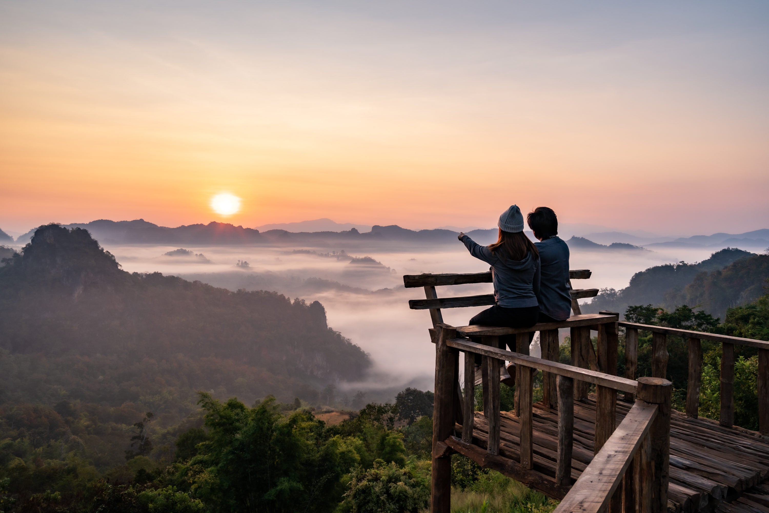 Young couple traveler looking at sea of mist and sunset over the mountain at Mae Hong Son Thailand