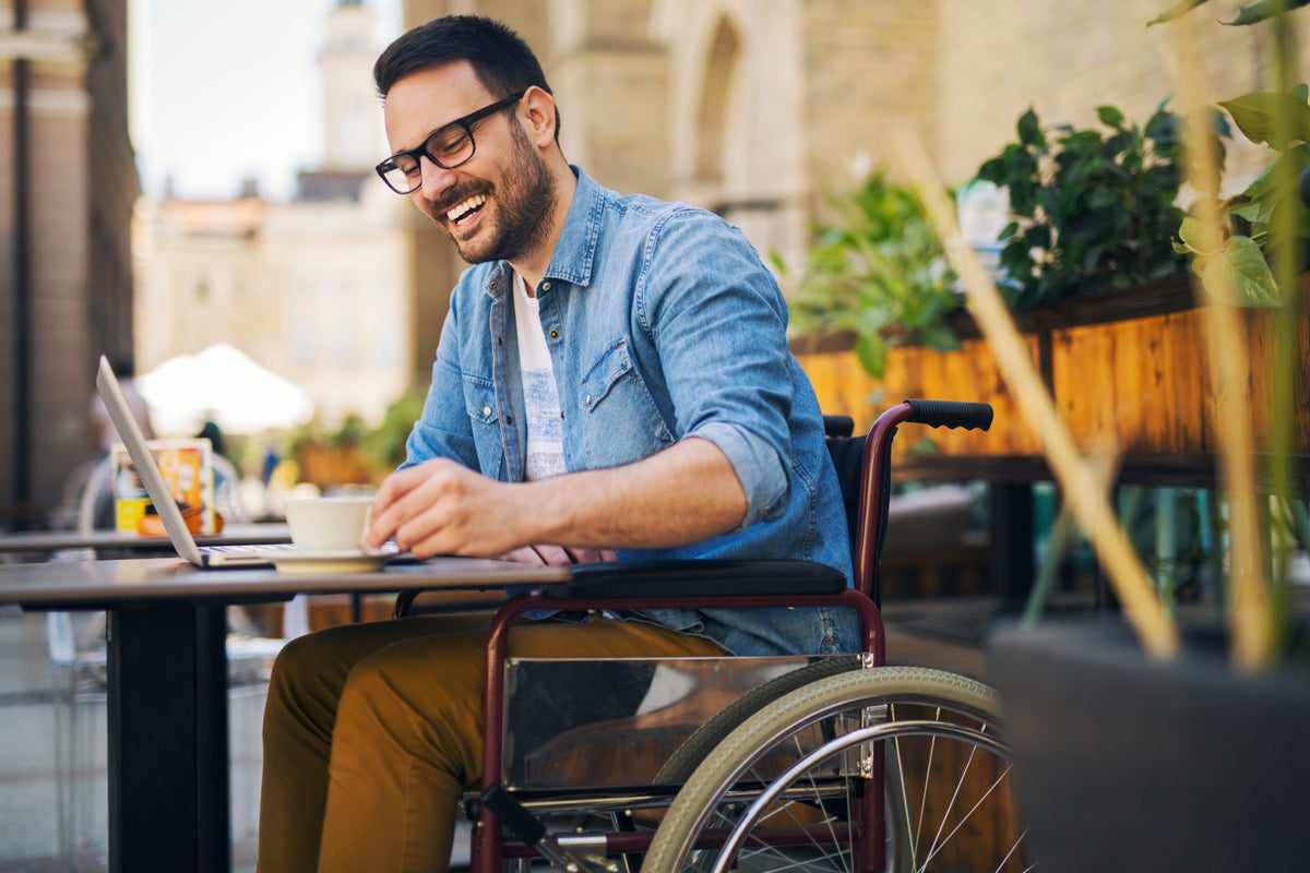 Man in wheelchair laughing at cafe with laptop