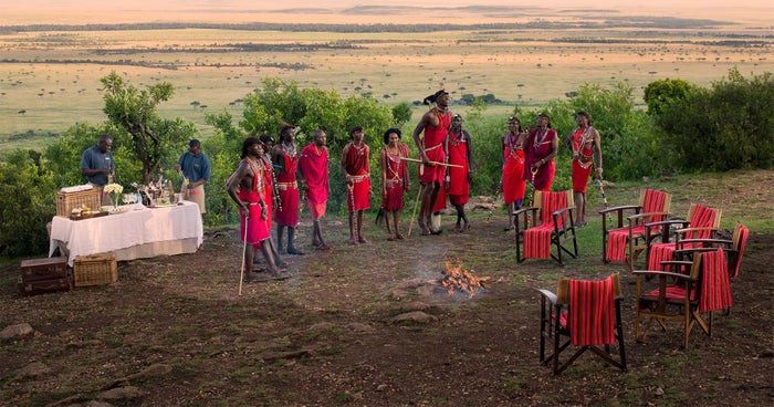 The Maasai people in the Maasai Mara Natural Reserve dressed in red and standing around a small fire. The Maasai people in the Maasai Mara Natural Reserve dressed in red and standing around a small fire.