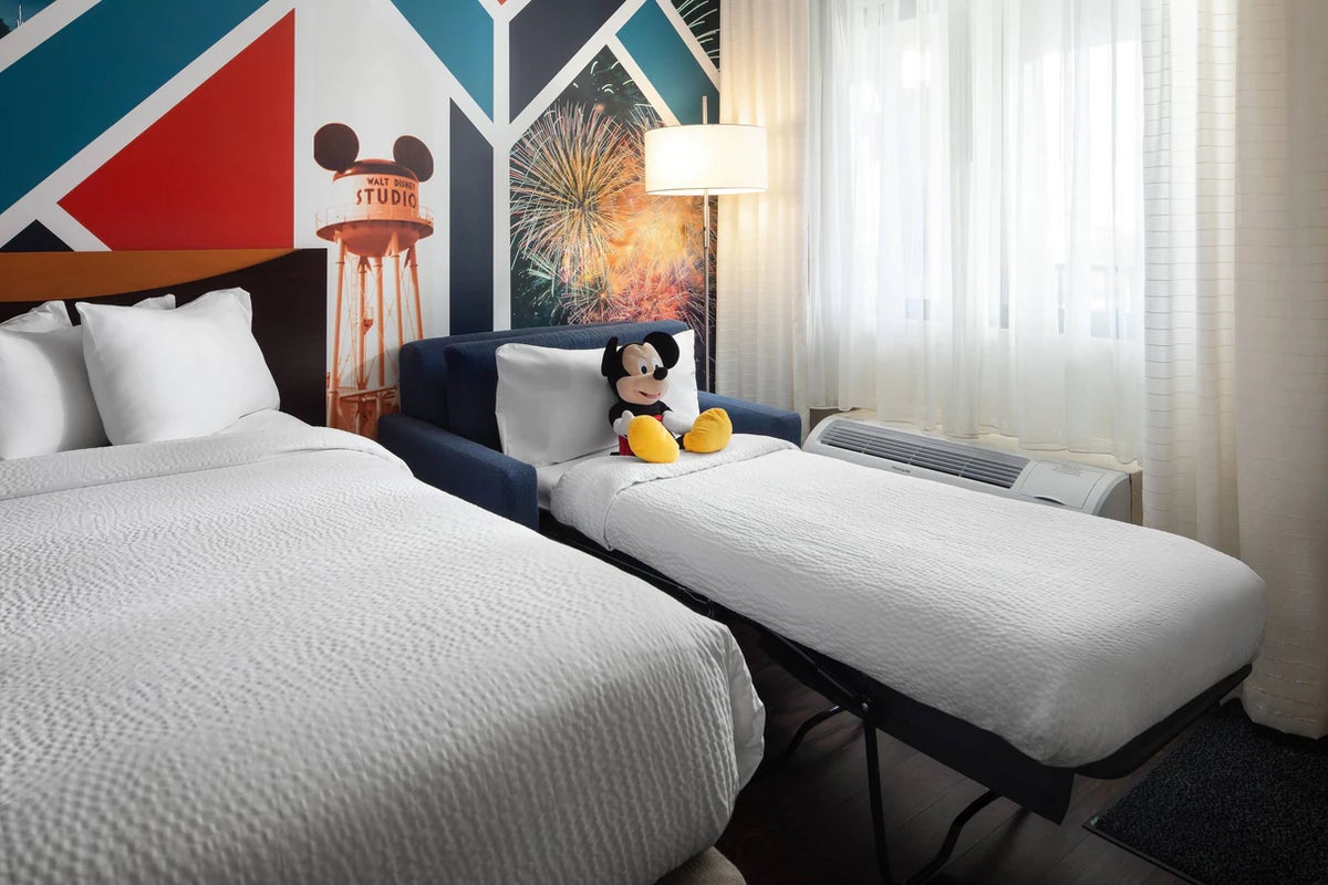A photo of a guestroom at Fairfiled Anaheim Resort shows a pullout sofa bed with a Mickey Mouse stuffed animal against a pillow.