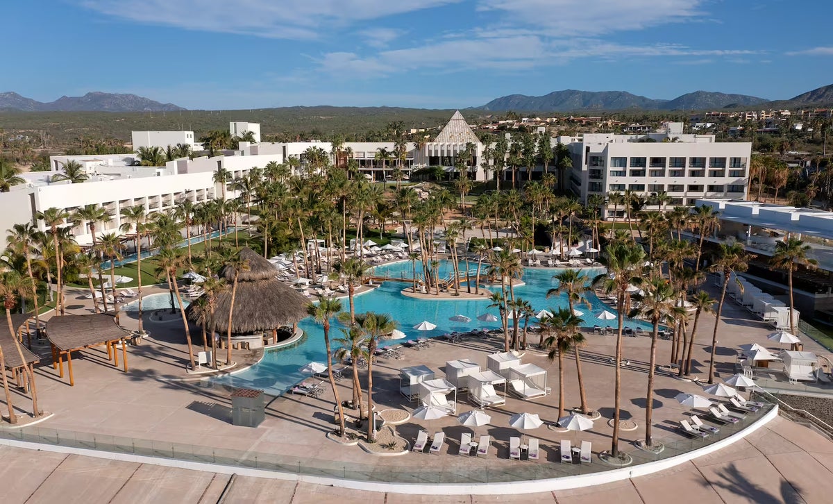The view of Paradisus Los Cabos's pool and hotel area surrounded by palm trees and ample lounge chairs.