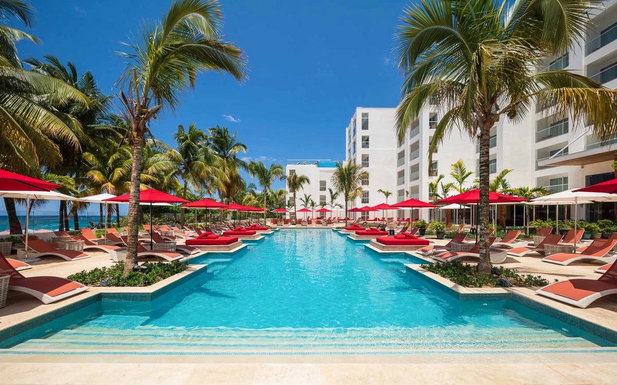 The pool area at S Hotel Jamaica surrounded by red umbrellas and lounge chairs with palm trees.