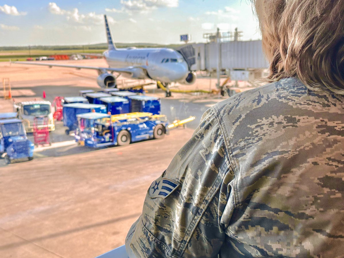 Military woman in airport looks out window at plane