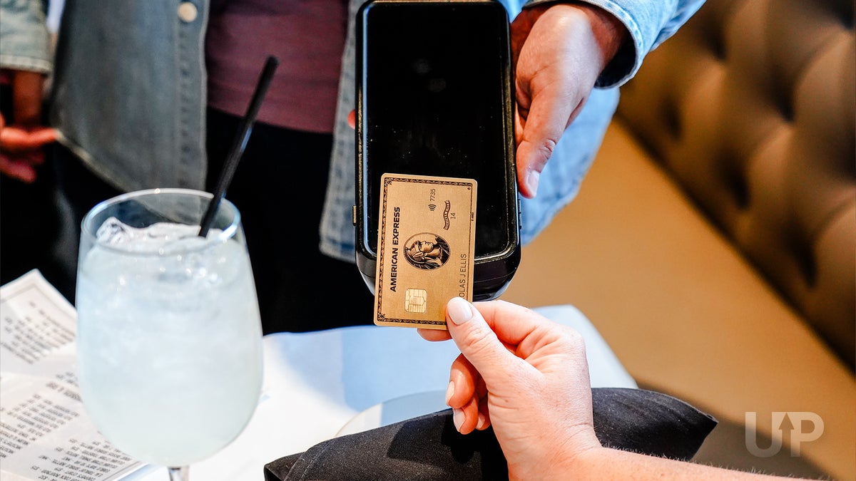 A person tapping an Amex Gold on a contactless payment terminal