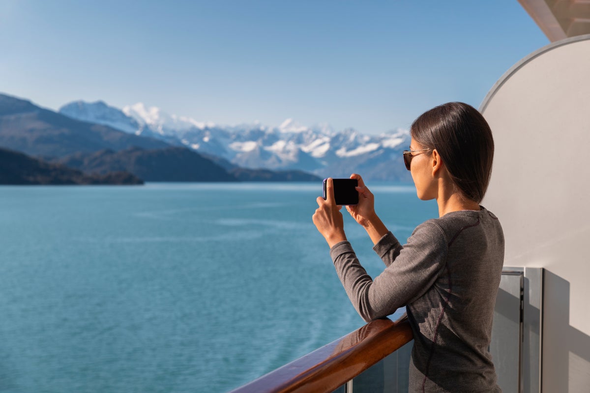 Woman takes picture of glaciers in Alaska from cruise ship balcony