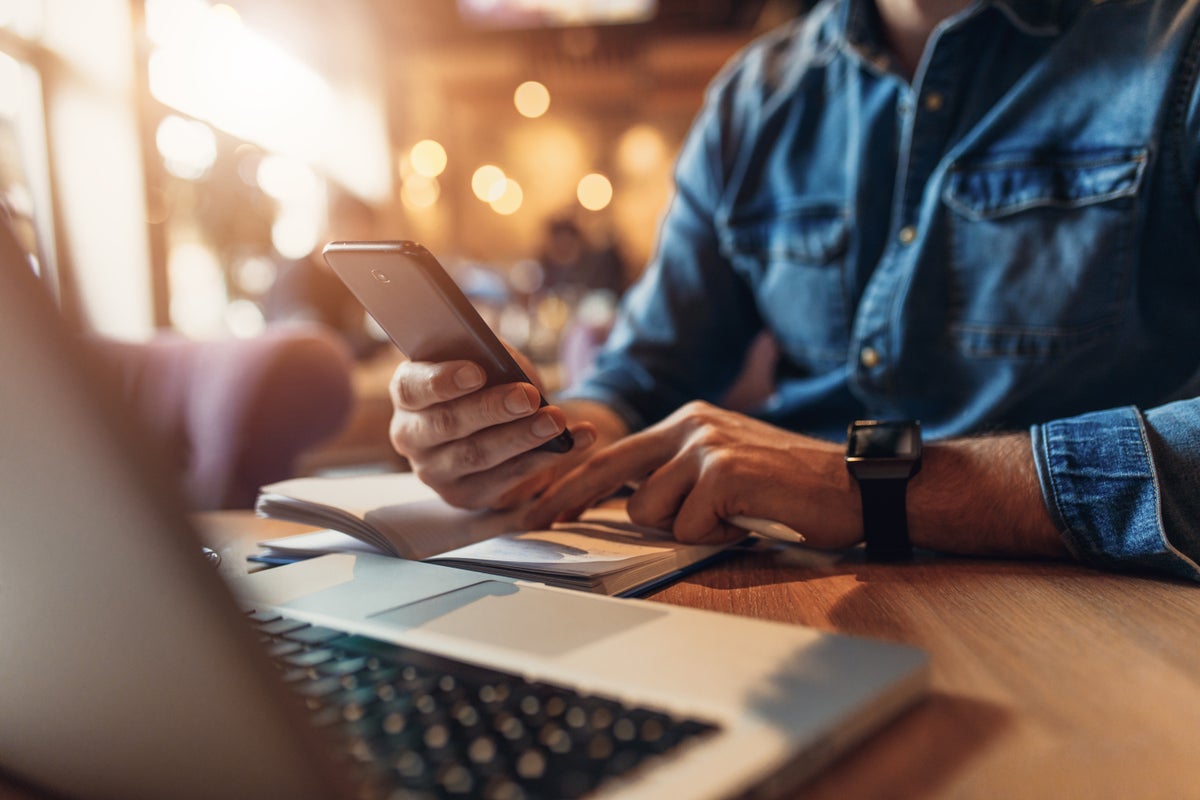 Close up of young man hand texting message on phone while sitting at cafe.